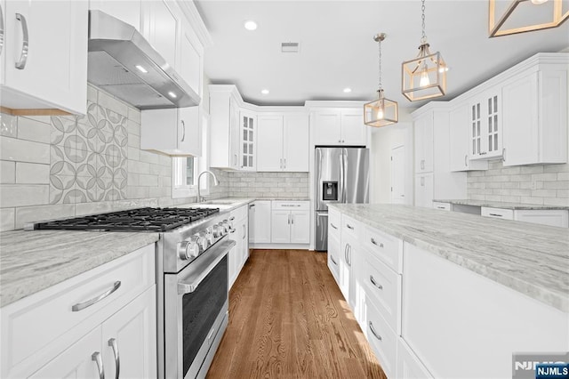 kitchen featuring stainless steel appliances, white cabinetry, glass insert cabinets, and wall chimney range hood