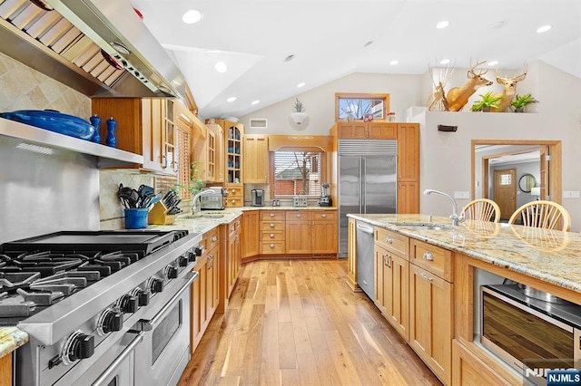 kitchen with lofted ceiling, extractor fan, light stone countertops, high end appliances, and glass insert cabinets