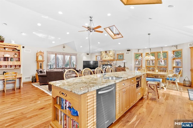 kitchen featuring stainless steel dishwasher, light brown cabinetry, open floor plan, an island with sink, and light stone countertops