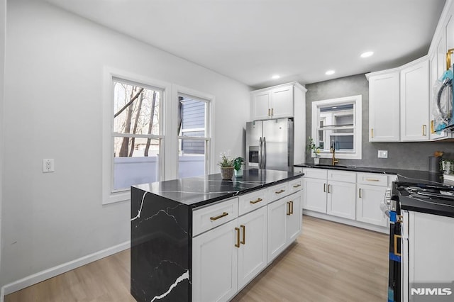 kitchen with white cabinets, dark countertops, stainless steel appliances, light wood-type flooring, and a sink