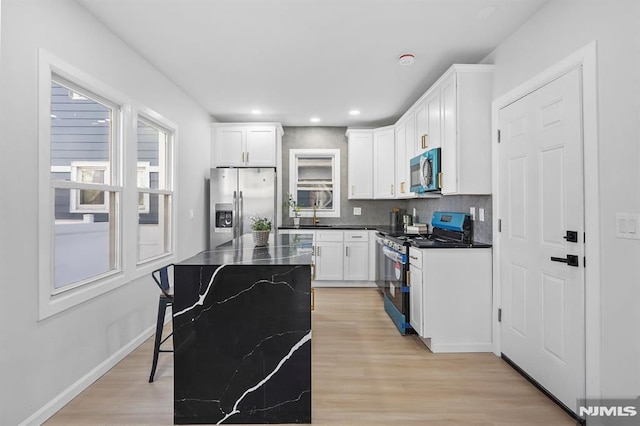 kitchen with tasteful backsplash, dark countertops, appliances with stainless steel finishes, light wood-style floors, and white cabinetry