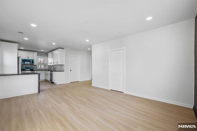 unfurnished living room with recessed lighting, a sink, light wood-style flooring, and baseboards