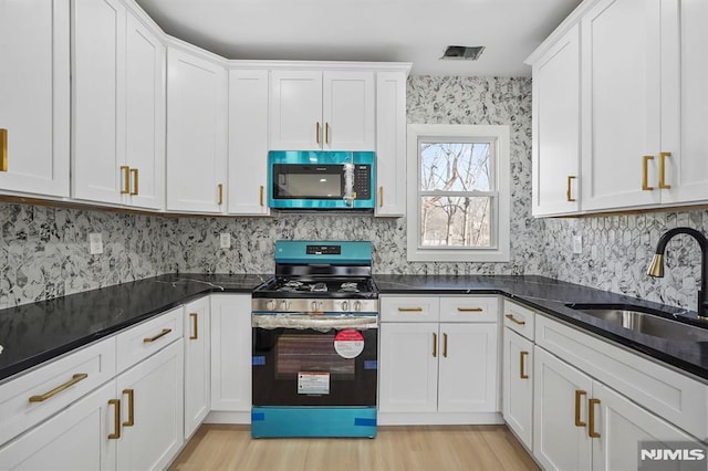 kitchen featuring stainless steel gas range oven, light wood-style flooring, a sink, and white cabinetry