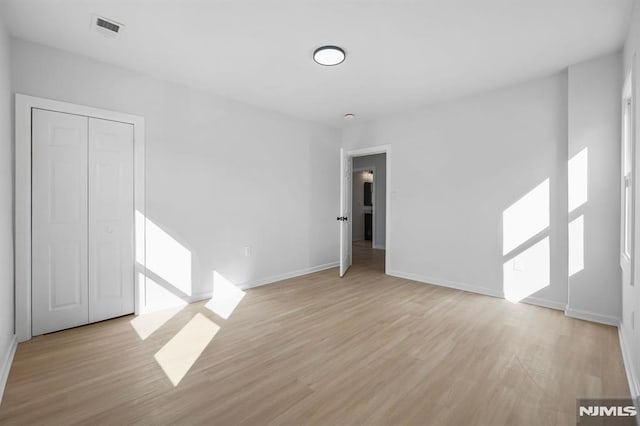 empty room featuring light wood-type flooring, visible vents, and baseboards