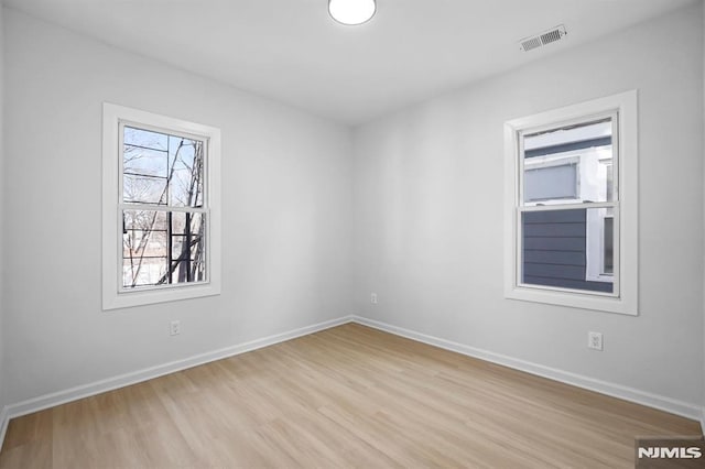 empty room featuring light wood-style floors, baseboards, and visible vents