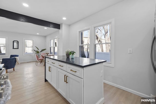 kitchen with light wood-style flooring, white cabinets, open floor plan, a center island, and dark countertops