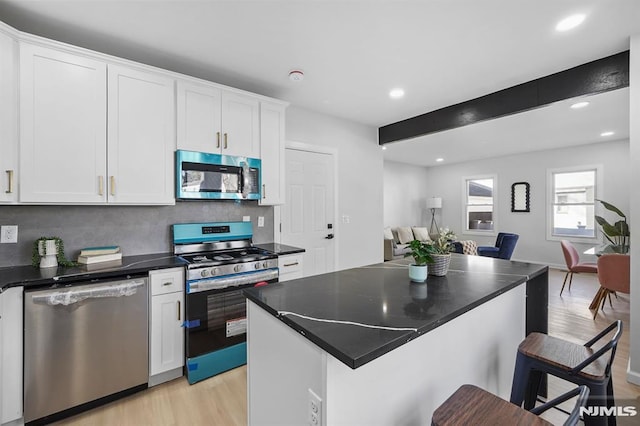 kitchen featuring appliances with stainless steel finishes, dark countertops, open floor plan, and white cabinets