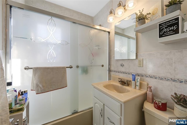 bathroom featuring toilet, combined bath / shower with glass door, tile walls, and vanity