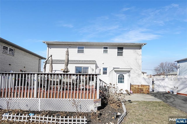 rear view of property featuring driveway, a wooden deck, a gate, and fence