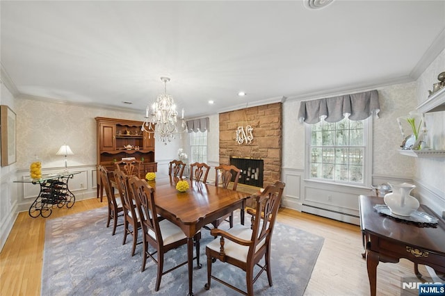 dining space with a stone fireplace, light wood-style flooring, a baseboard heating unit, ornamental molding, and wainscoting