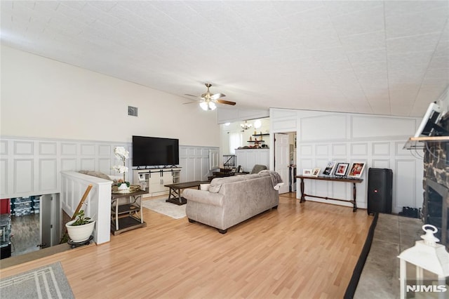 living area featuring vaulted ceiling, wood finished floors, a fireplace with flush hearth, and a decorative wall