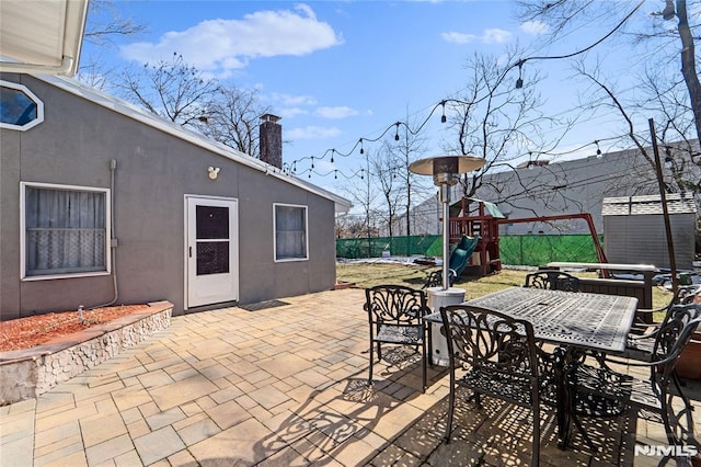 view of patio / terrace featuring outdoor dining area, a playground, fence, and a storage shed