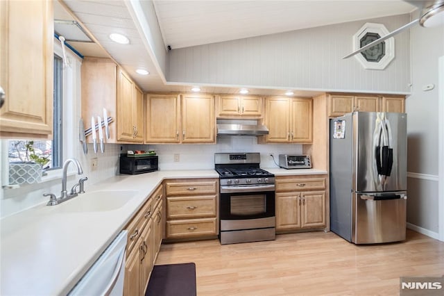 kitchen with light countertops, light brown cabinetry, appliances with stainless steel finishes, a sink, and under cabinet range hood