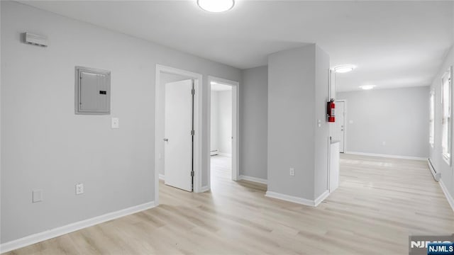 empty room featuring light wood-style flooring, electric panel, baseboards, and baseboard heating