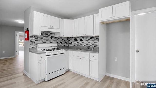 kitchen featuring under cabinet range hood, a sink, white cabinetry, light countertops, and white gas range