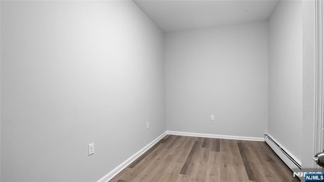 empty room with a baseboard radiator, light wood-style flooring, and baseboards