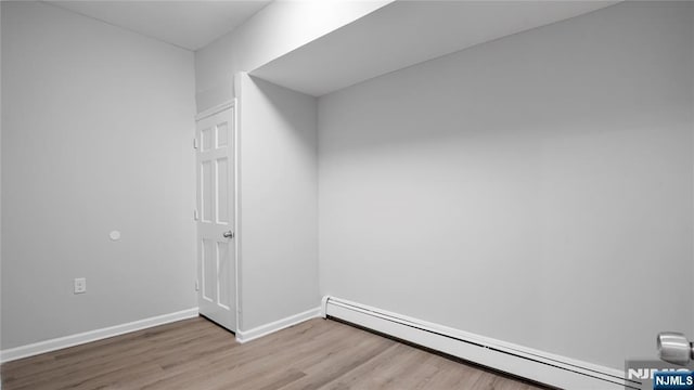 unfurnished room featuring a baseboard heating unit, light wood-style floors, and baseboards