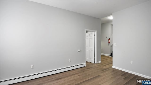 unfurnished room with a baseboard heating unit, dark wood finished floors, and baseboards