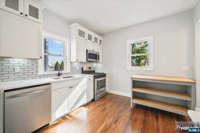 kitchen featuring stainless steel appliances, a sink, white cabinetry, tasteful backsplash, and glass insert cabinets