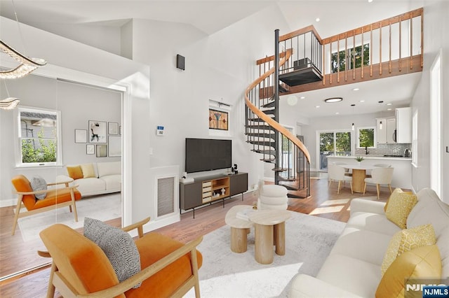 living room with high vaulted ceiling, stairway, light wood-type flooring, and baseboards