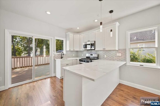 kitchen with stainless steel appliances, hanging light fixtures, light wood-style floors, white cabinets, and a peninsula