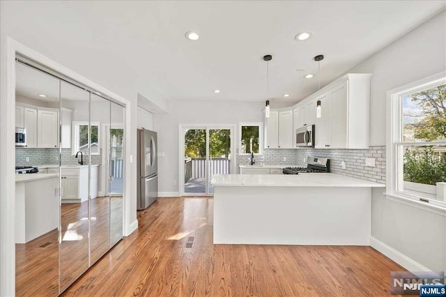 kitchen with white cabinets, a peninsula, light stone countertops, stainless steel appliances, and pendant lighting