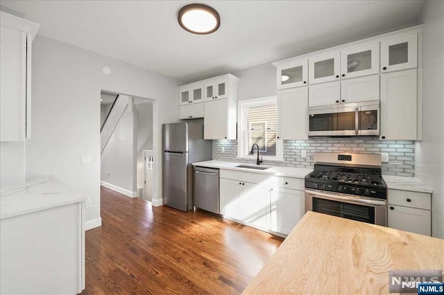 kitchen with stainless steel appliances, dark wood-style flooring, a sink, white cabinetry, and glass insert cabinets