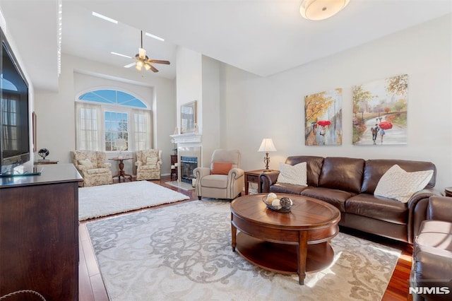 living area with a fireplace with flush hearth, a ceiling fan, and wood finished floors