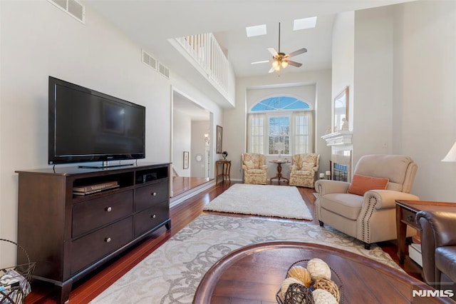 living room featuring a skylight, ceiling fan, visible vents, and dark wood-type flooring