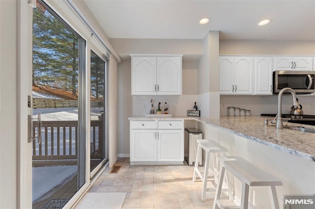 kitchen with recessed lighting, stainless steel microwave, white cabinets, a sink, and light stone countertops