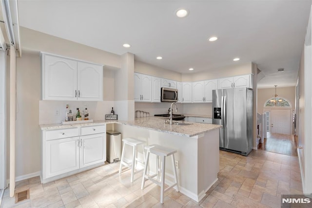 kitchen featuring light stone counters, stainless steel appliances, white cabinets, a sink, and a peninsula