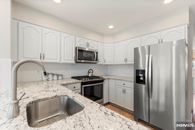 kitchen with light stone countertops, white cabinetry, appliances with stainless steel finishes, and a sink