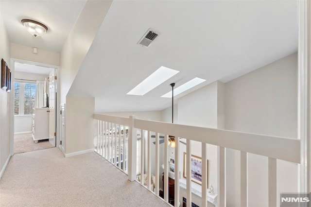 hall featuring vaulted ceiling with skylight, visible vents, baseboards, and light colored carpet