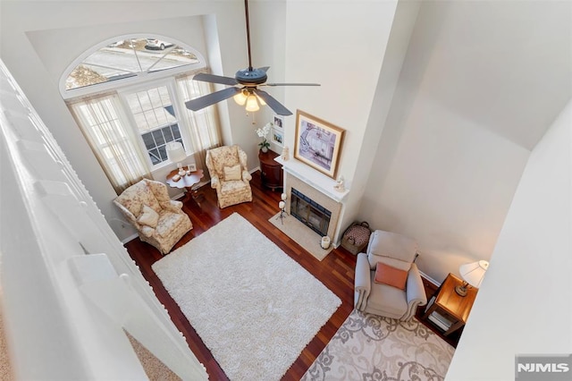 living area with a fireplace, wood finished floors, a towering ceiling, and a ceiling fan