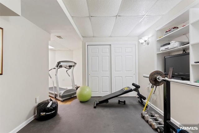 exercise room with a paneled ceiling, visible vents, and baseboards