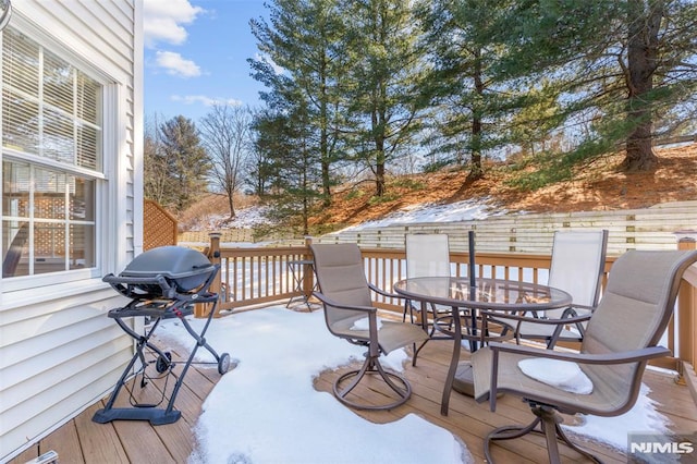 snow covered deck with outdoor dining space and grilling area