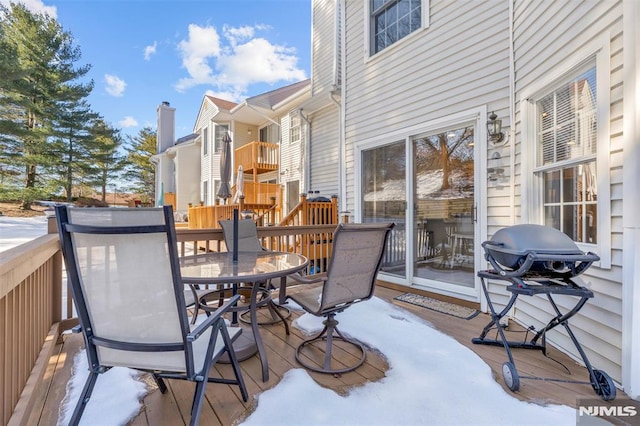 snow covered deck featuring outdoor dining space and a grill