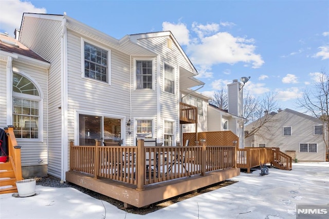 snow covered back of property with a wooden deck