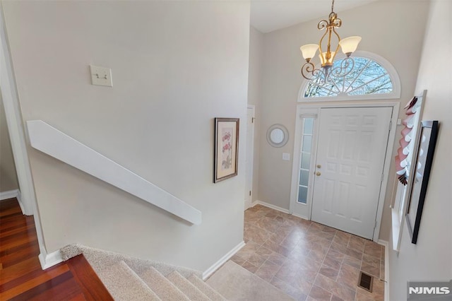 foyer entrance featuring baseboards, visible vents, stairway, a high ceiling, and a notable chandelier