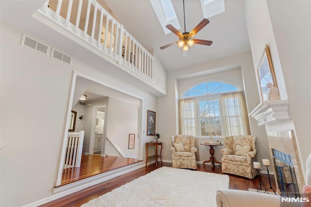 sitting room featuring dark wood-type flooring, a glass covered fireplace, a high ceiling, and a skylight