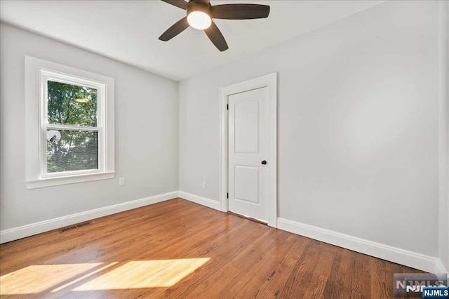 empty room featuring a ceiling fan, visible vents, light wood-style flooring, and baseboards