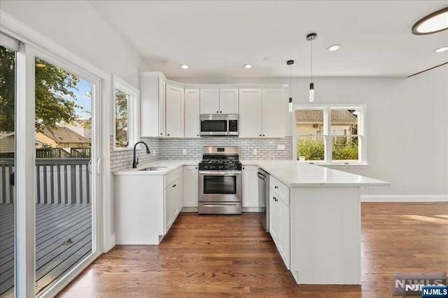 kitchen featuring a peninsula, appliances with stainless steel finishes, white cabinets, and pendant lighting