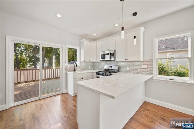 kitchen with a peninsula, white cabinetry, appliances with stainless steel finishes, light wood finished floors, and decorative light fixtures