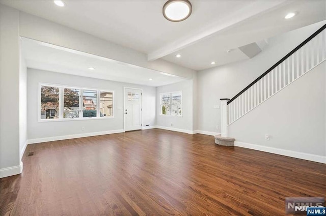 unfurnished living room with a wealth of natural light, stairway, beam ceiling, and baseboards