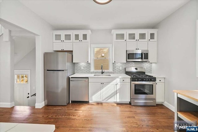 kitchen featuring stainless steel appliances, light countertops, glass insert cabinets, white cabinets, and a sink