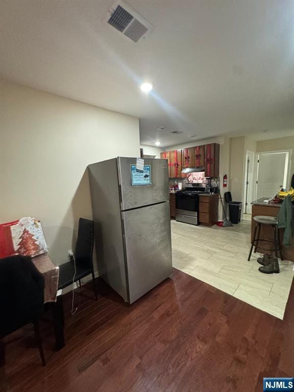 kitchen with reddish brown cabinets, light wood finished floors, visible vents, and appliances with stainless steel finishes