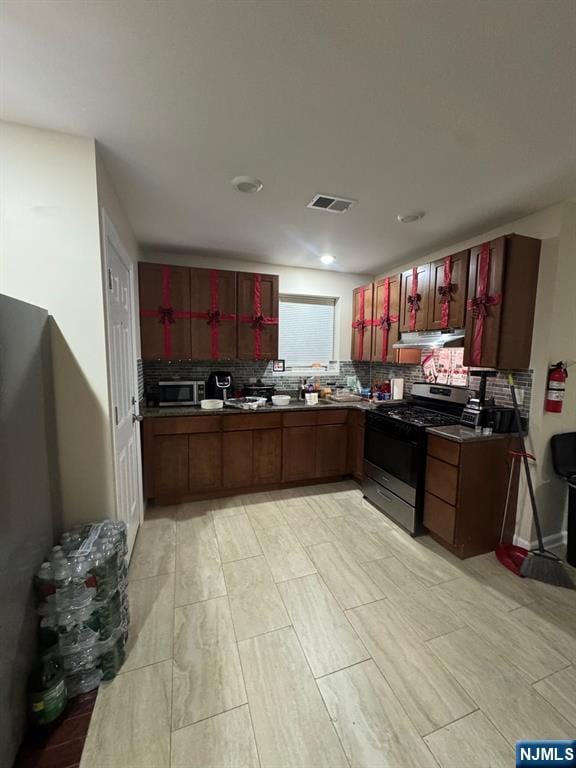 kitchen with appliances with stainless steel finishes, dark countertops, backsplash, and under cabinet range hood