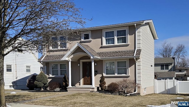 traditional home featuring roof with shingles, fence, and stucco siding