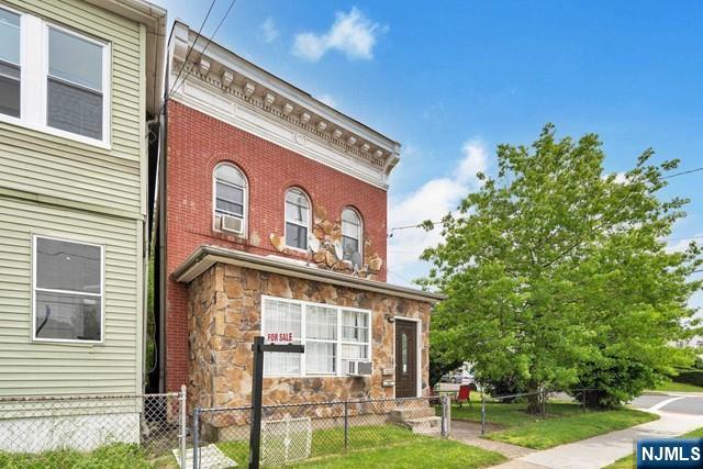 italianate-style house with stone siding, fence, cooling unit, a front lawn, and brick siding