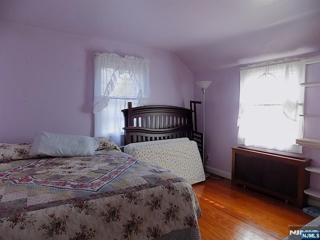 bedroom featuring vaulted ceiling, multiple windows, radiator heating unit, and wood finished floors